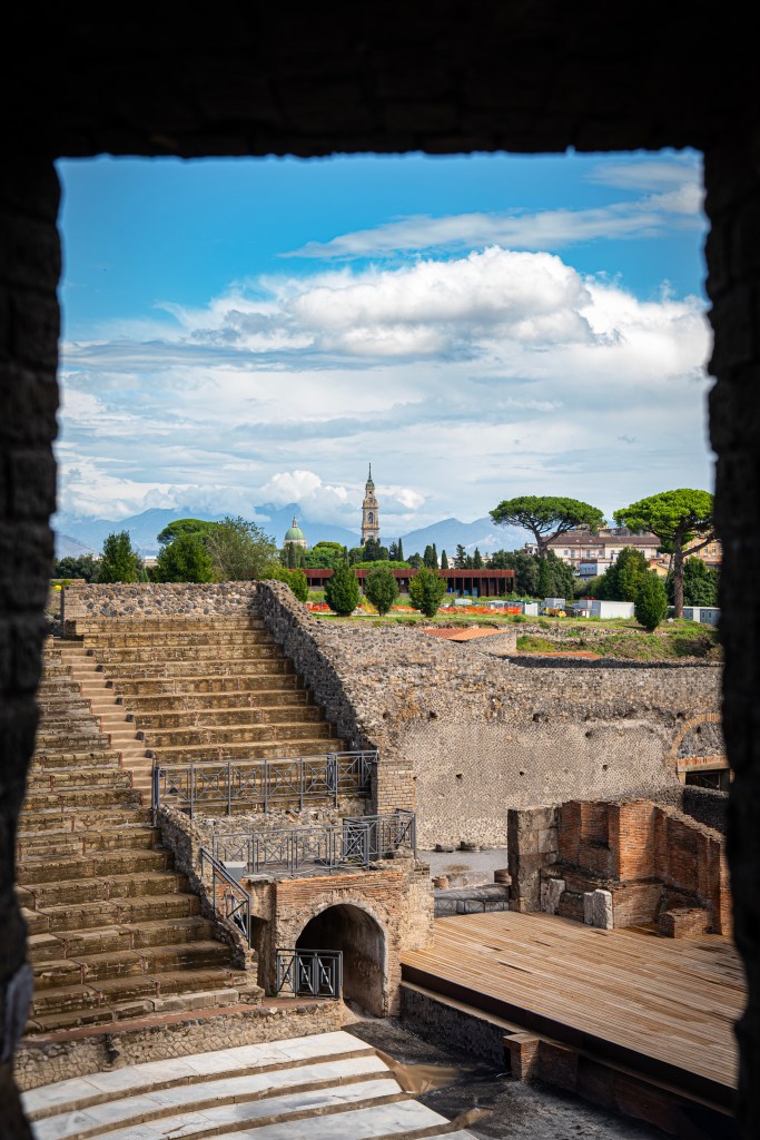 A unique view in the city of Pompeii, contrasting the ruins of an ancient, once buried city, with the modern cityscape of the surrounding area.